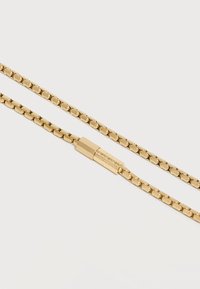 Κολιέ με χρυσούς τόνους και αλυσίδα κουτιού, με κυλινδρικό κούμπωμα που φέρει γεωμετρικό μοτίβο σε λευκό φόντο.