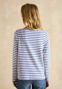 Pikad varrukad, ümar kaelusega topp horisontaalsete siniste ja valgete triipudega, pehme, veniva kangaga ja vabalt lasuv vorm.