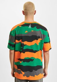 Majica s kratkim rukavima od pamuka s camo uzorkom u zelenoj, narančastoj, crnoj i sivoj boji. Sadrži mali logotip na leđima.