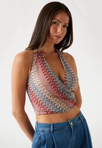 Knitted halter crop top featuring a multicolored wavy pattern in shades of red, blue, and cream. Soft texture with a plunging neckline.