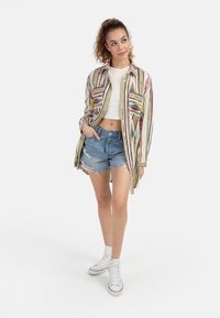 Camicia leggera a righe con pattina button front, due tasche sul petto, top bianco cropped, pantaloni shorts in denim strappati e sneakers alte bianche.