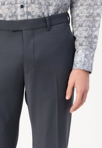 Pantalon gris foncé à coupe droite, avec une texture lisse, des poches latérales et des passants de ceinture. La taille est soigneusement finie.