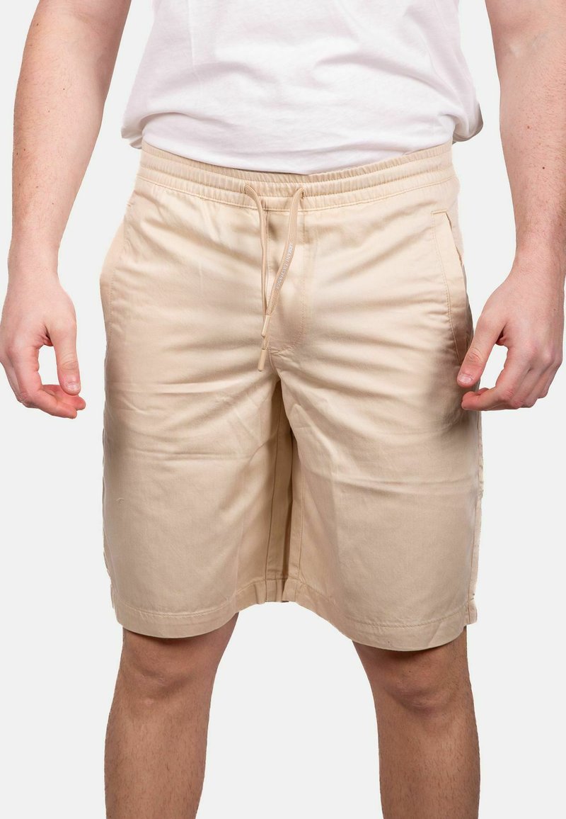 Pantaloni corti beige realizzati in tessuto leggero, con vita elastica e cordino. Presentano tasche laterali e un design snello.