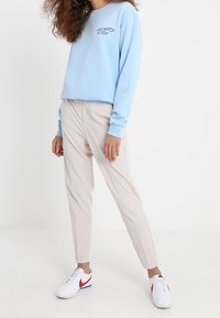 Jasnoniebieski sweter z okrągłym dekoltem z graficznym napisem, zestawiony z beżowymi spodniami o kroju dopasowanym i białymi trampkami z czerwonymi i niebieskimi akcentami.