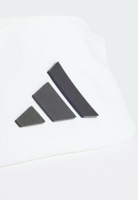 Gorra blanca con una superficie de tela lisa, que presenta un prominente logo negro de Adidas compuesto por tres rayas inclinadas.