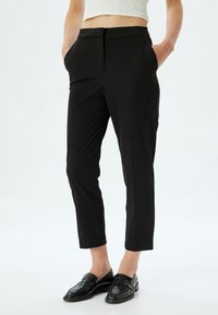 Zwarte op maat gemaakte broeken met een slim fit, middelhoge taille, zijzakken en een gladde textuur. Draagt met glanzende zwarte instappers.