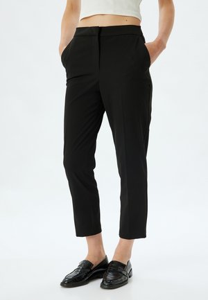 Black tailored trousers with a slim fit, mid-rise waist, side pockets, and a smooth texture. Worn with glossy black loafers.