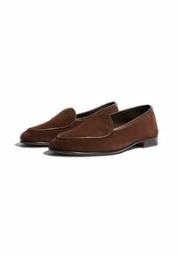 Mocassini in suede marrone con punta arrotondata e un sottile design cucito. Presentano un tacco basso e un bordo a contrasto lungo i lati.