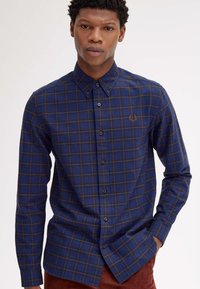 Camicia a quadri blu navy con maniche lunghe, colletto button-down e dettagli marroni. Caratterizzata da logo sul petto e una finitura in tessuto testurizzato.