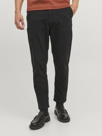 Schwarze Baumwoll-Chinos mit schmaler Passform, ausgestattet mit Seitentaschen, einem Reißverschluss und einem leicht zulaufenden Bein, kombiniert mit polierten schwarzen Slippern.