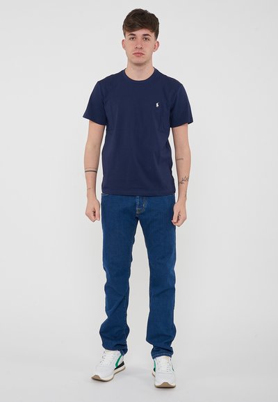 T-shirt in cotone blu navy con collo a giro e piccolo logo ricamato. Abbinato a jeans in denim blu e sneakers bianche con accenti verdi.