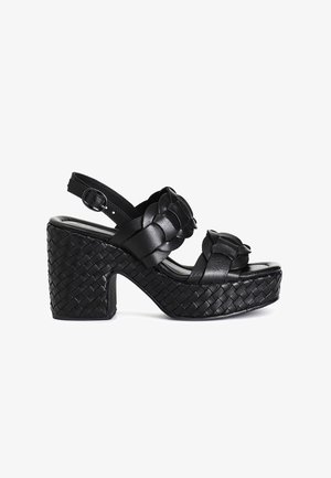 Sandale negre din piele cu talpă înaltă, cu curele împletite, textură țesută pe toc și curea ajustabilă la gleznă.