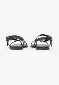 Zwarte leren sandalen met kruislings gespen en een vlakke zool. Verstelbare sluiting met een gouden accent. Glad, minimalistisch ontwerp.