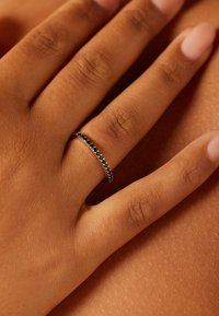 Zwarte ring met kleine edelstenen, gedragen aan een hand. De band heeft een gladde textuur en een slank ontwerp, dat de stenen in een rij benadrukt.