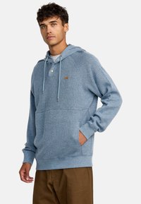 Light blue, ribbed hoodie with a drawstring, button detail, kangaroo pocket, and long sleeves. Fabric has a soft texture.
