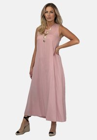 Długa, bezrękawna różowa sukienka z dekoldem w kształcie litery V, złotymi guzikami z przodu oraz luźnym krojem. Połączona z czarnymi i beżowymi butami na koturnie.