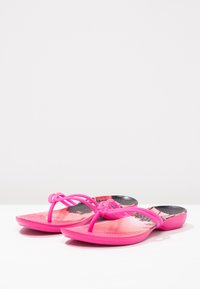 Klart rosa flip-flop-sandaler med tunna remmar och texturerade fotbäddar med svarta och rosa mönster på en vit yta.