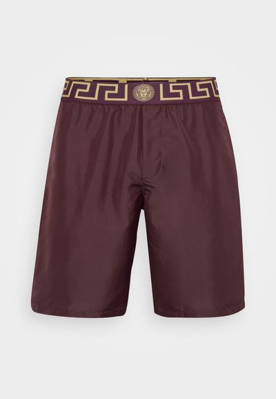 Κόκκινες μαγιό τσέπες με χρυσό λογότυπο ελληνικού κλειδιού στη μέση και κεντρικό χρυσό έμβλημα. Κατασκευασμένα από μαλακό, ελαφρύ ύφασμα με άνετη εφαρμογή.