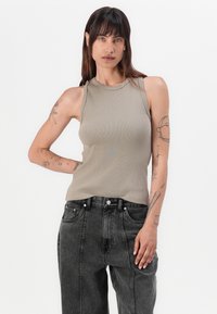 Pilkas juostelėmis dekoruotas tank topas su aukštu apykakle, derinamas su aukšto liemens juodais džinsais. Modelis turi matomų rankų tatuiruočių.