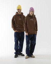 Felpe marroni con tasche frontali, indossate sopra jeans blu con un motivo sbiadito a forma di foglia. Berretti gialli e rosa completano gli abiti.