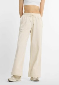 Pantalon de survêtement beige clair à jambes larges avec une ceinture élastique et un cordon de serrage, fabriqué en tissu doux, avec un style minimaliste et une marque discrète.