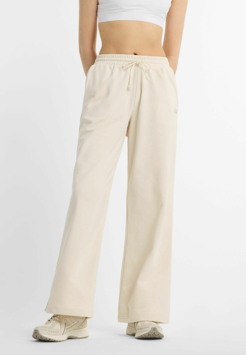 Pantalon de survêtement beige clair à jambes larges avec une ceinture élastique et un cordon de serrage, fabriqué en tissu doux, avec un style minimaliste et une marque discrète.
