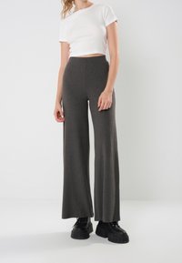 Grå ribbade vida byxor med hög midja, tillsammans med en vit kortärmad t-shirt och kraftiga svarta platåskor.