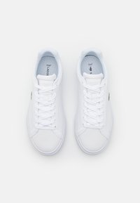 White sneakers with a smooth, synthetic upper, round toe, flat sole, lace-up closure, and a small green crocodile logo on the side.