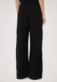 Svarta cargobyxor med vida ben, som har två sidofickor och två bakfickor, gjorda av mjuk och slät tyg.