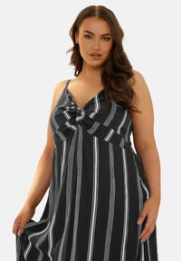 Randig svart-och-vit klänning med V-ringning, knytdetalj fram och tunna axelband, med ett flödande tygtextur.