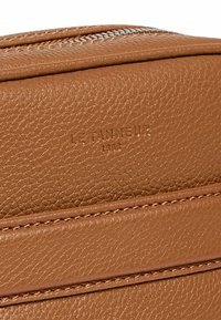 Braune, strukturiertes Lederhandtasche mit Reißverschluss, mit eingeprägtem Markennamen und kontrastierenden Nähten. Kompakte rechteckige Form.