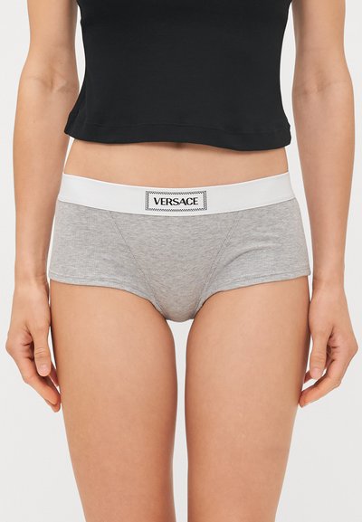 Harmaat ribbipaidat, joissa on valkoinen elastinen vyötärösauma, jossa on musta Versace-logo. Klassinen leikkaus ja sileä pinta tarjoavat mukavuutta.