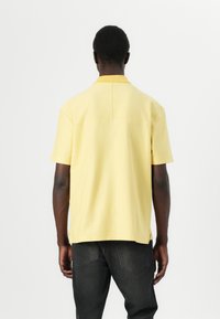 Kortermet gul polo-skjorte med rett kant, baksemsdetail og myk tekstur. Skjorten er matchende med mørke jeans.