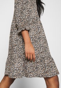 Blumendruckkleid in Schwarz, Weiß und Orange. Kurze Puffärmel und rüschensaum. Leichter Stoff mit fließendem Design.