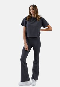 Szary krótki t-shirt z szerokimi rękawami w połączeniu z dopasowanymi szarymi spodniami w dzwony. Oba wykonane z miękkiego materiału, noszone z białymi trampkami.