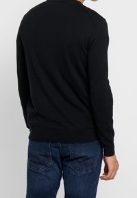 Black knitted sweater with long sleeves, crew neck, and ribbed hem, paired with blue denim jeans featuring back pockets and stitching details.