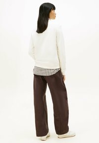 White sweatshirt with ribbed cuffs, layered over a checkered shirt. Paired with loose brown pants and white sneakers. Neutral background.