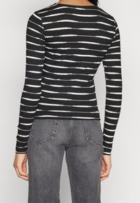 Långärmad topp med svart- och vitrandigt mönster, tillverkad av ribbat tyg. Bakifrån visas en figurnära design och rund halsringning.