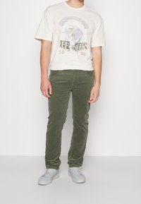 Camiseta gráfica de algodón en color crema con diseño de paloma. Pantalones de pana verde oliva. Zapatillas blancas. Diseño sencillo con ajuste relajado.