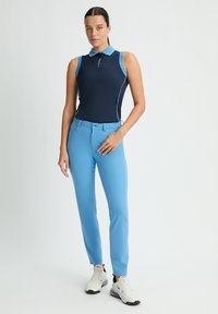 Marinblå ärmlös polo med ljusblå krage och detaljer. Ljusblå figurnära byxor med framfickor. Grå atletiska sneakers.