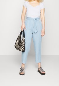 Ljust blå högmidjade byxor med slipsbälte, i kombination med en vit ribbad topp och en handväska i svart och vitt vävt mönster. Svarta sandaler med blommönster.