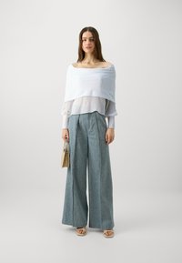 Lett og hvit av-shoulder topp lagd over en tynn bluse, kombinert med høyt midje, vide lyseblå bukser og beige sandaler.