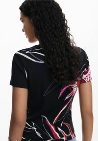 Top nero a costine con motivi floreali in rosso, rosa e bianco. Maniche corte e design aderente mettono in risalto i colori vivaci.