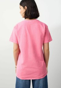 Short-sleeve, crew-neck T-shirt in bright pink cotton, featuring a relaxed fit and soft texture. Back view shows minimal stitching detail.