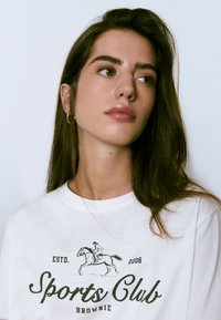 Camiseta de algodón blanca con gráficos en negro que presentan un jinete, "Club Deportivo" y el texto "ESTD. 2006", con cuello redondo y mangas cortas.