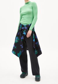 Ribbade gröna långärmade tröja, svarta byxor och en flerfärgad blommig sjal. Sjalen har nyanser av blått och grönt mot en svart bakgrund.