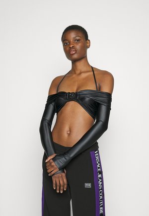 Μαύρο κοντό μπλουζάκι με σχέδιο που αφήνει τους ώμους ακάλυπτους και κεντρική λεπτομέρεια από μέταλλο, συνδυασμένο με μαύρο παντελόνι που έχει μοβ πλαϊνές ρίγες και λογότυπο.