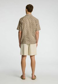 Camicia a maniche corte, con un motivo marrone e beige, abbinata a pantaloni corti leggeri beige. Tessuto morbido e vestibilità rilassata. Retro semplice con colletto.