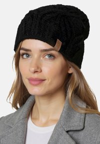 Fekete kötött sapka textúrált mintával és egy kis bőrcímkével. A sapka laza, oversized kialakítású.