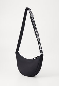 Borsa a tracolla nera con forma curva, realizzata in tessuto liscio. Caratterizzata da una tracolla con logo e testo bianco a contrasto e una chiusura con cerniera.